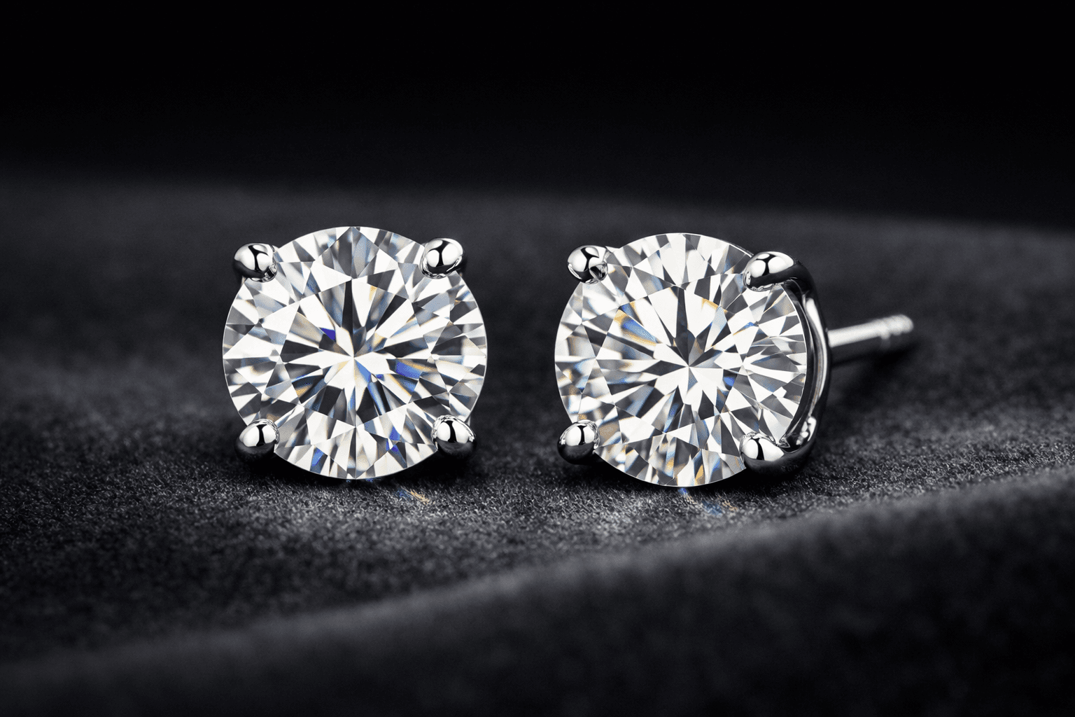Brilliant round-cut diamond stud earrings in four-prong silver settings resting on dark velvet fabric.